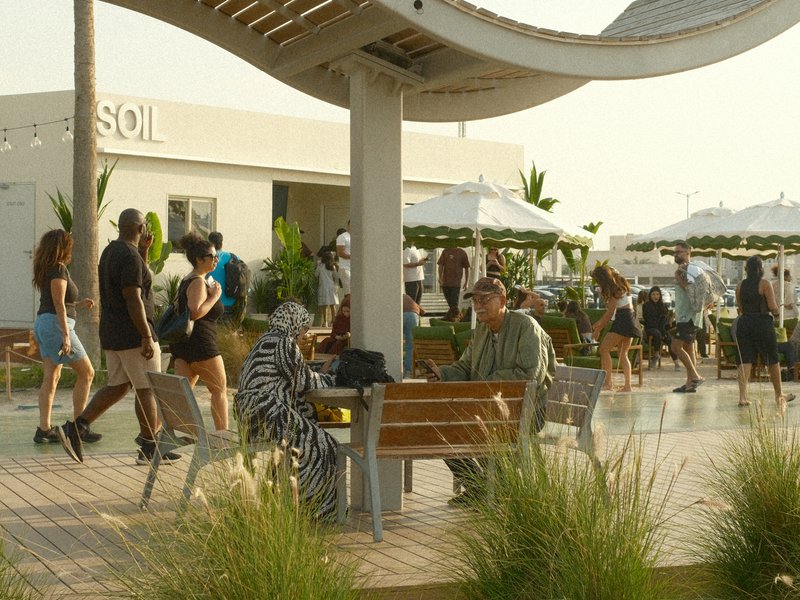 A bustling outdoor scene with people walking, sitting on benches, and enjoying a sunny day.