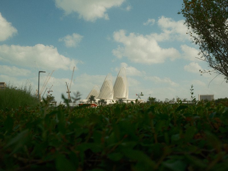 View of modern architecture peeking above greenery under a partly cloudy sky.