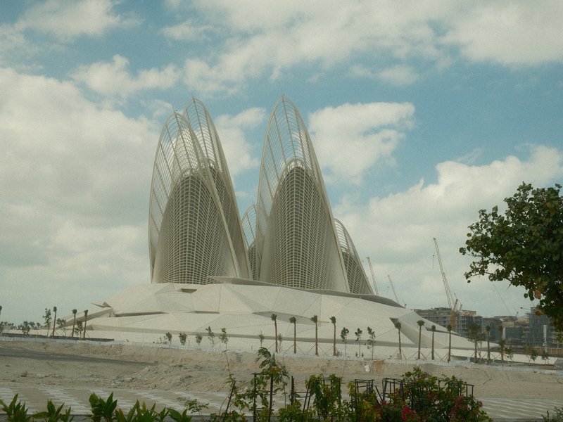 A modern architectural structure with pointed roofs against a cloudy sky, surrounded by greenery.