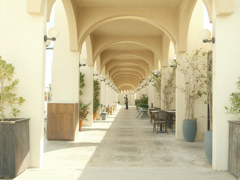A long corridor with arches, lined with potted plants and outdoor seating, creating a serene atmosphere.
