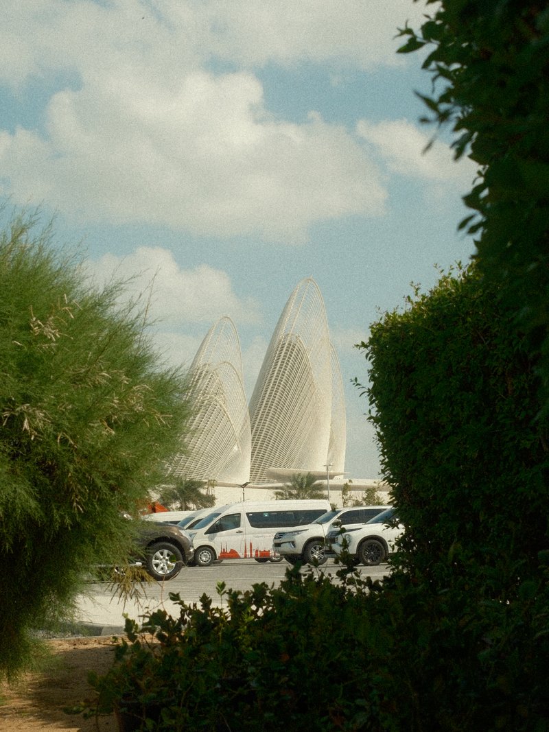 Two modern architectural structures resembling lotus flowers, framed by greenery and a cloudy sky.