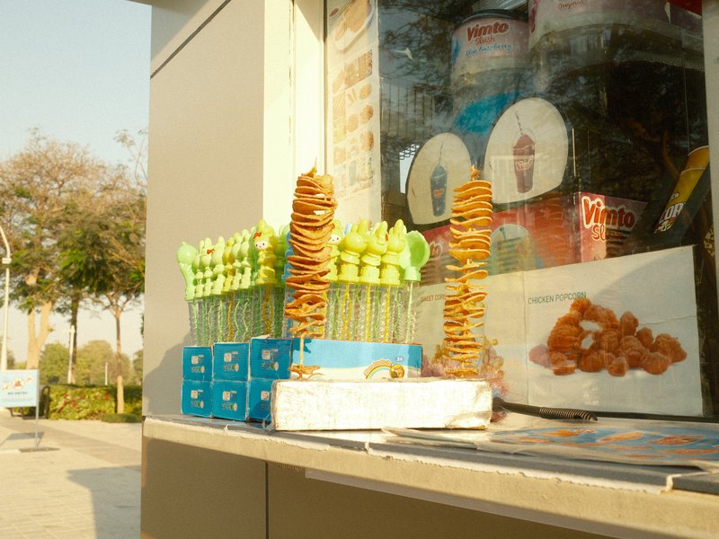 A colorful display of snacks and drinks at a street vendor's stall in a sunny outdoor setting.