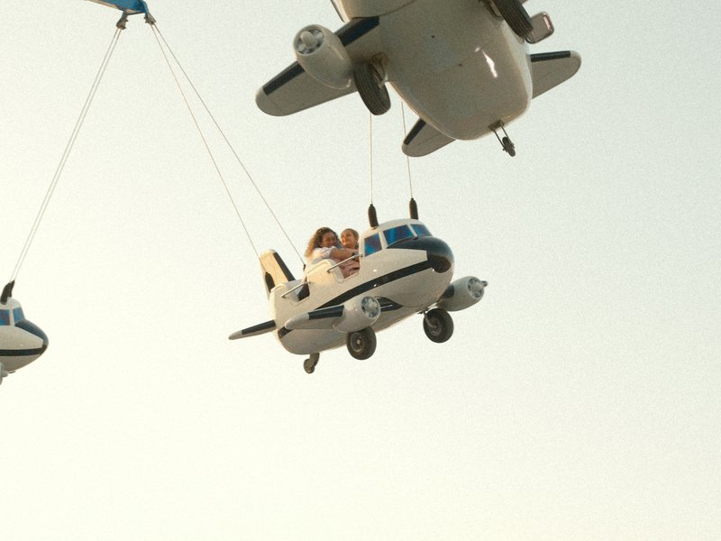 Three toy airplanes suspended in the air against a pale sky, with two figures in one plane.