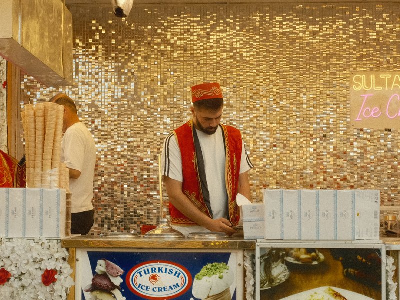 A vendor in traditional attire prepares food at a vibrant stall with a sparkling backdrop.