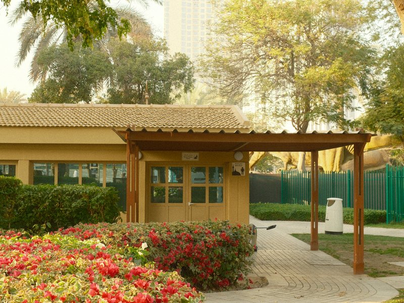 A small yellow building with a wooden awning surrounded by colorful flowers and greenery.