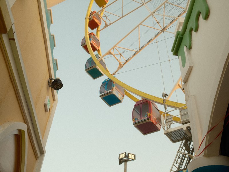 View of a colorful ferris wheel framed by two buildings in a fairground setting.