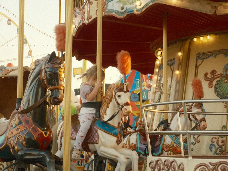 A carousel with colorful horses and a girl taking a photo, illuminated by festive lights.