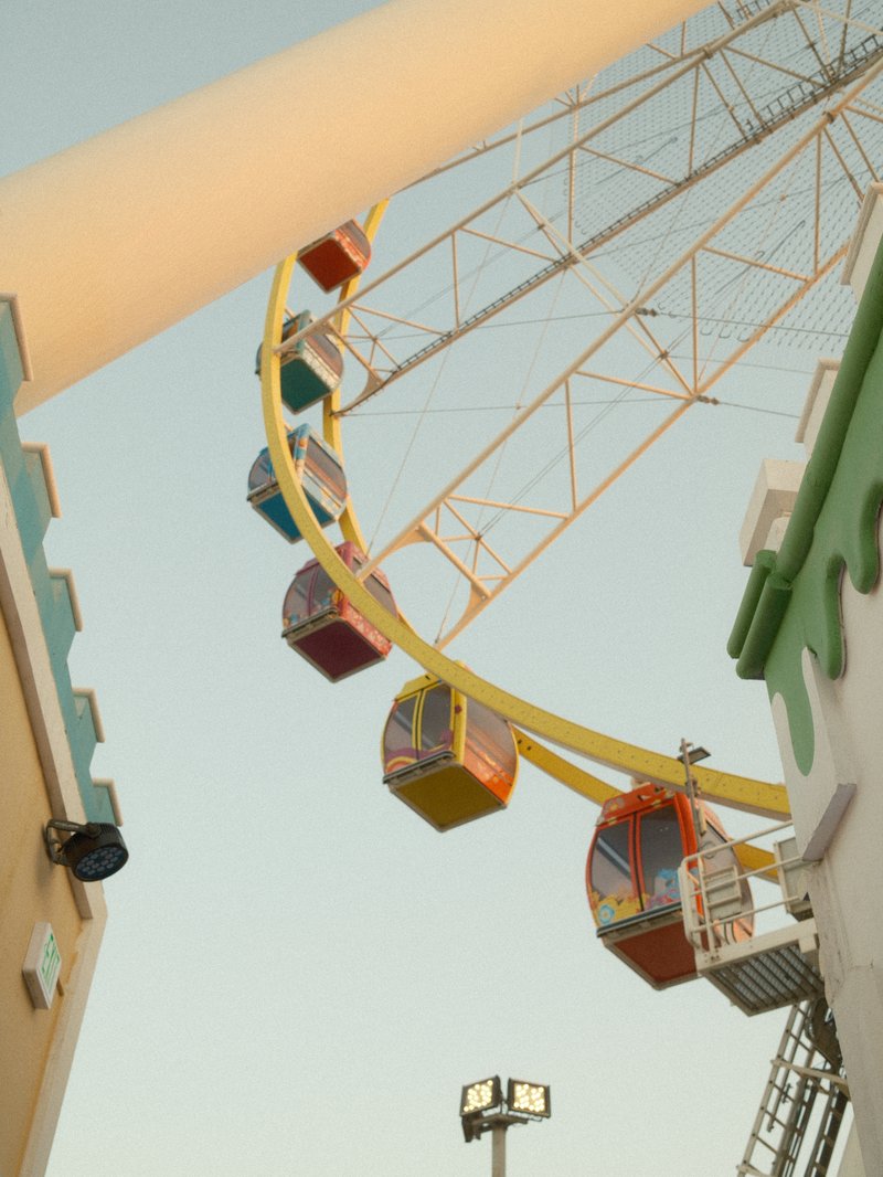 Colorful gondolas of a ferris wheel against a clear sky, with architectural elements in the foreground.