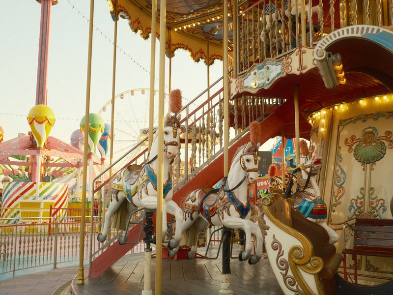 A colorful carousel with ornate horses, set in a vibrant amusement park during golden hour.