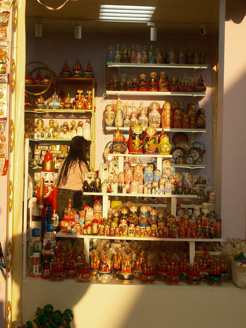 A woman browsing a colorful display of decorative dolls and figurines in a shop.