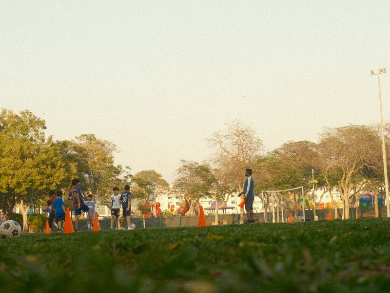 A soccer practice scene with players and cones on a grassy field during golden hour.