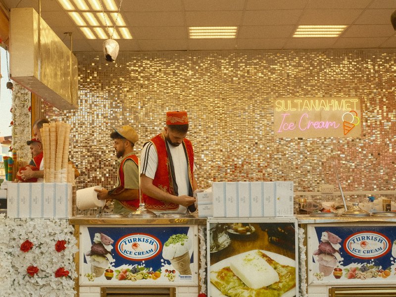 Two vendors preparing food at a colorful market stall with a sparkling background.