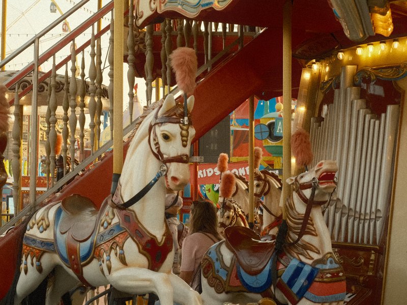 A colorful carousel with ornate horses and a child standing beside them, vibrant decorations in the background.
