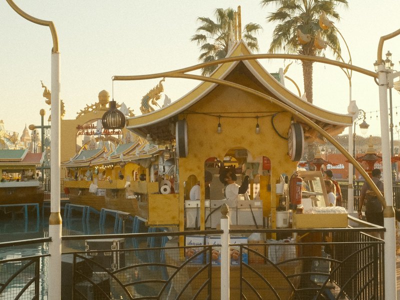 A vibrant waterfront scene featuring a colorful pavilion with palm trees in the background during sunset.