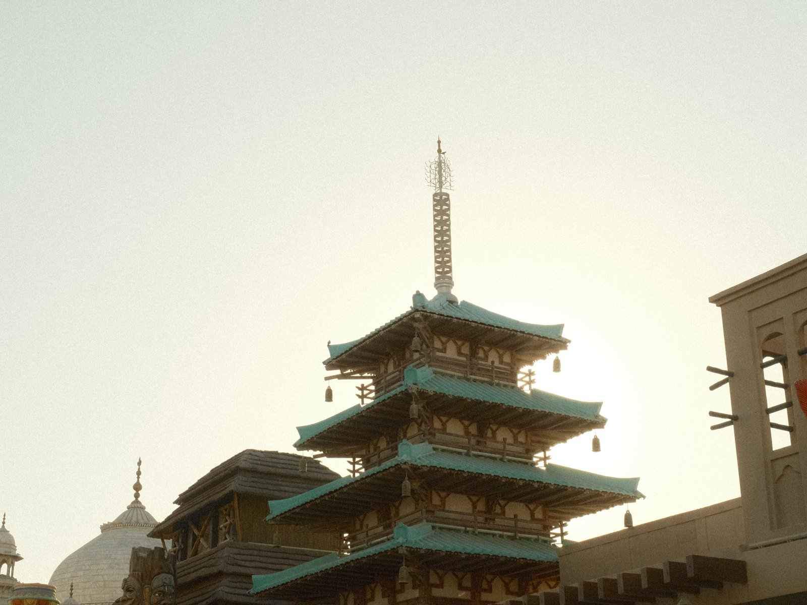 Silhouette of a pagoda against a bright sky, with buildings in the foreground.