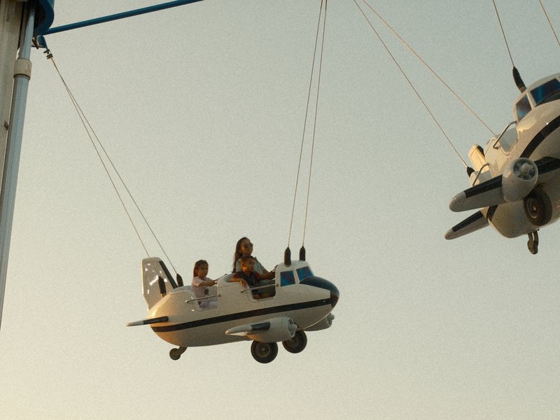 Two children enjoying a ride in airplane-shaped swings during sunset.