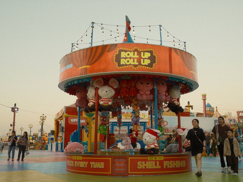 A colorful carnival game booth with plush toys and visitors in a festive setting.