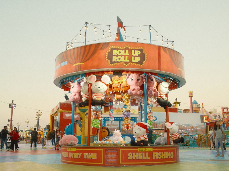 A colorful carnival game booth with stuffed animals hanging, set against a bright sky.