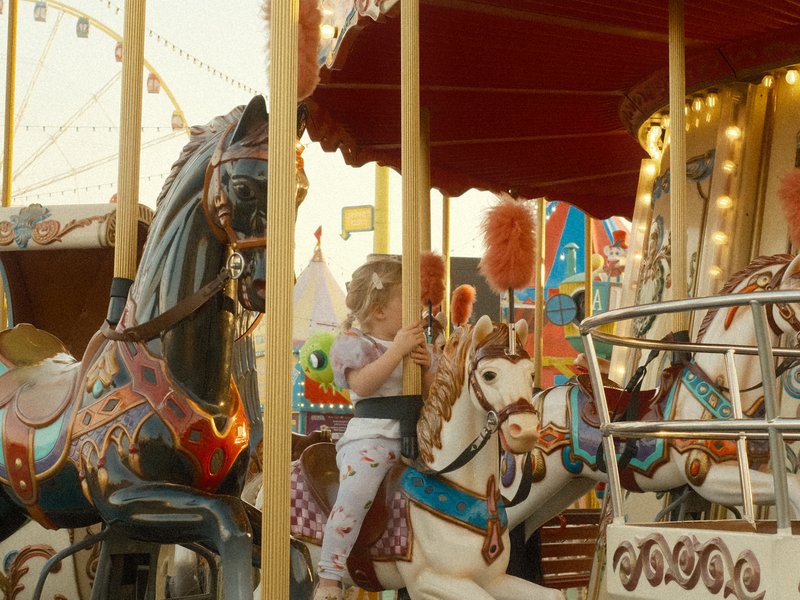 A child riding a carousel horse at a carnival, surrounded by colorful decorations and lights.