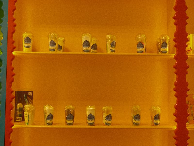 A brightly colored display shelf with jars containing a creamy substance, set against an orange background.
