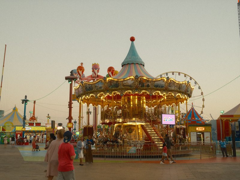 A brightly lit carousel at dusk surrounded by colorful amusement park attractions.