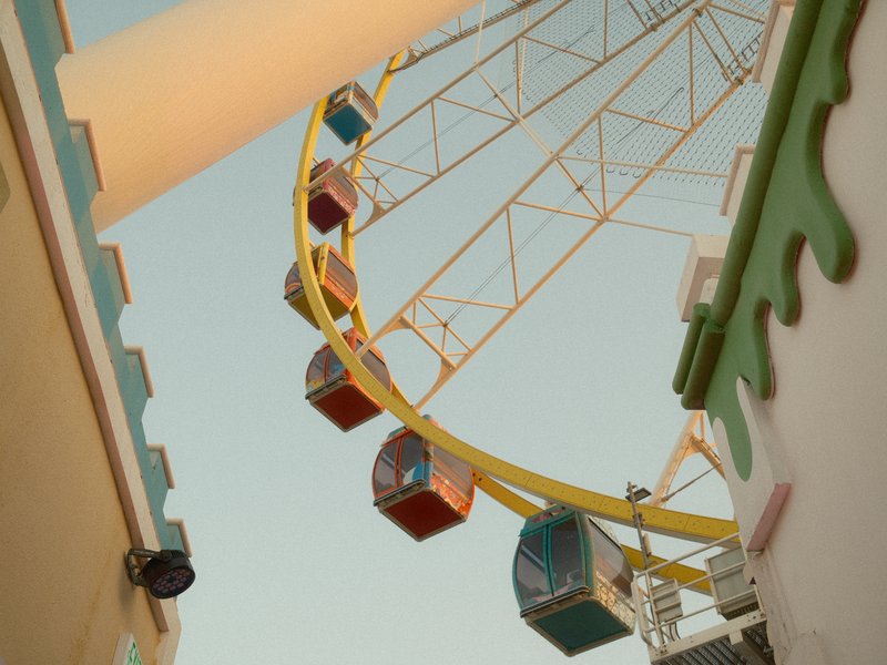 A colorful ferris wheel with cabins against a clear sky, framed by buildings.