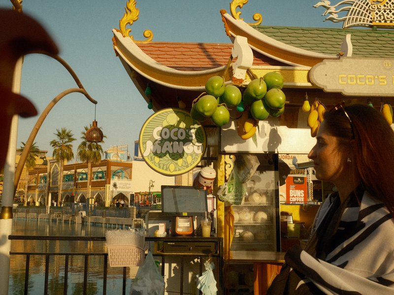 A woman stands near a colorful market stall with green limes, reflecting a vibrant outdoor atmosphere.