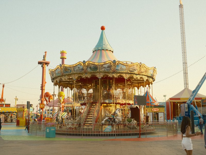 A vintage carousel at an amusement park during golden hour, surrounded by colorful rides.