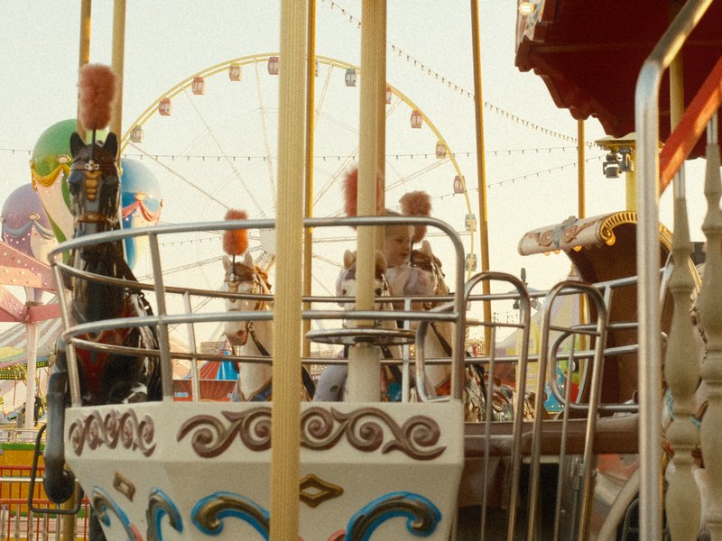 A colorful carnival ride with a ferris wheel in the background during golden hour.