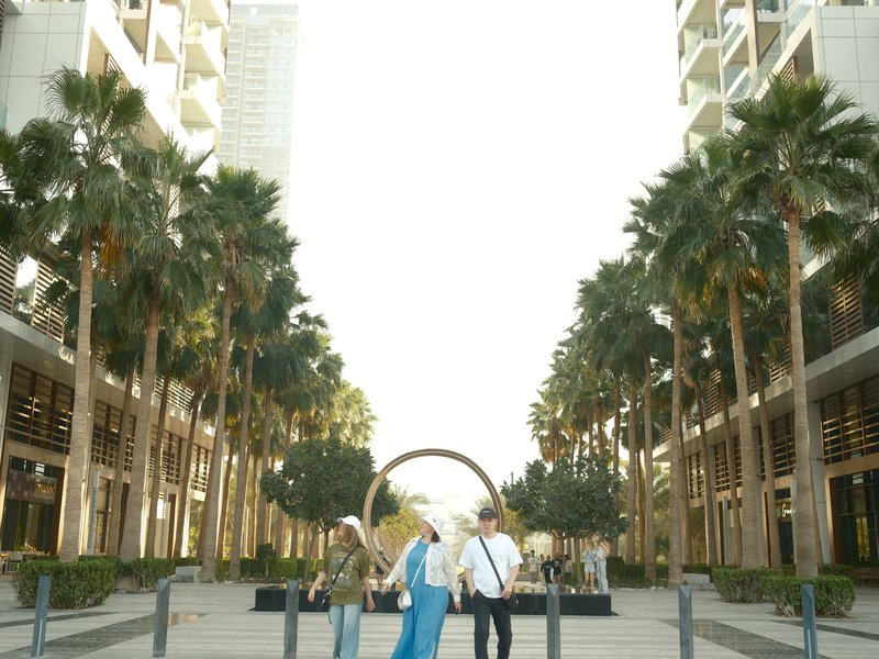 Two people walking in a palm-lined urban area with modern buildings in the background.