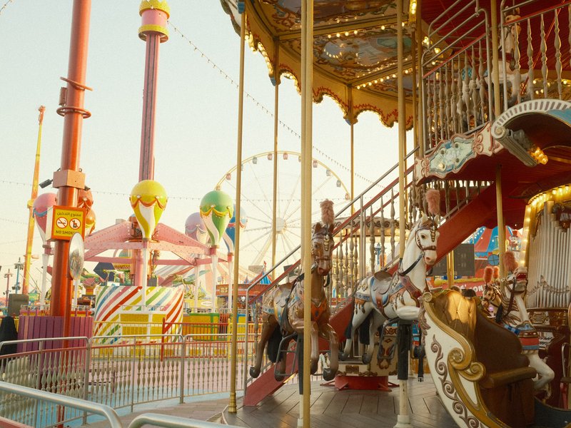 A colorful carousel with horses at an amusement park, featuring a ferris wheel in the background.