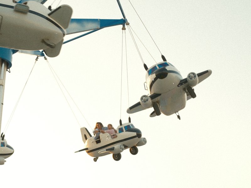 Colorful toy airplanes hanging from a crane against a pale sky.
