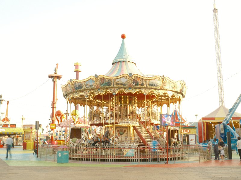 A vintage carousel with ornate decorations and colorful horses at an amusement park during the day.