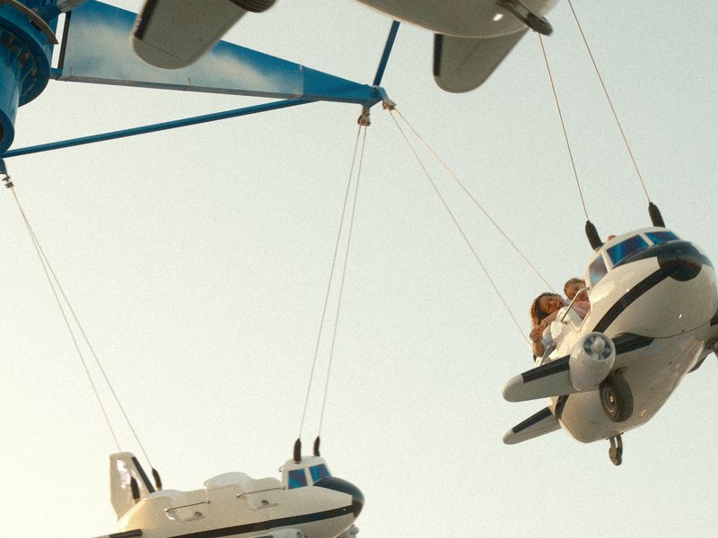 Two children enjoying a ride in toy airplanes suspended from a carnival ride against a clear sky.