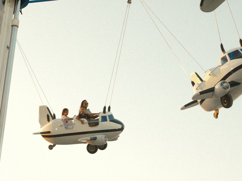 Two children enjoying a ride in small airplane-shaped seats against a clear sky.