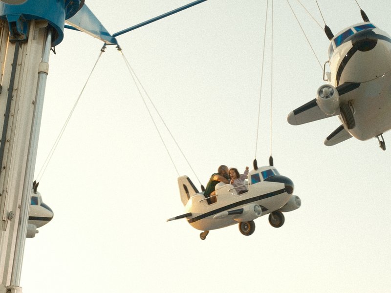 Children enjoying a carnival ride in airplane-shaped seats against a sunset sky.