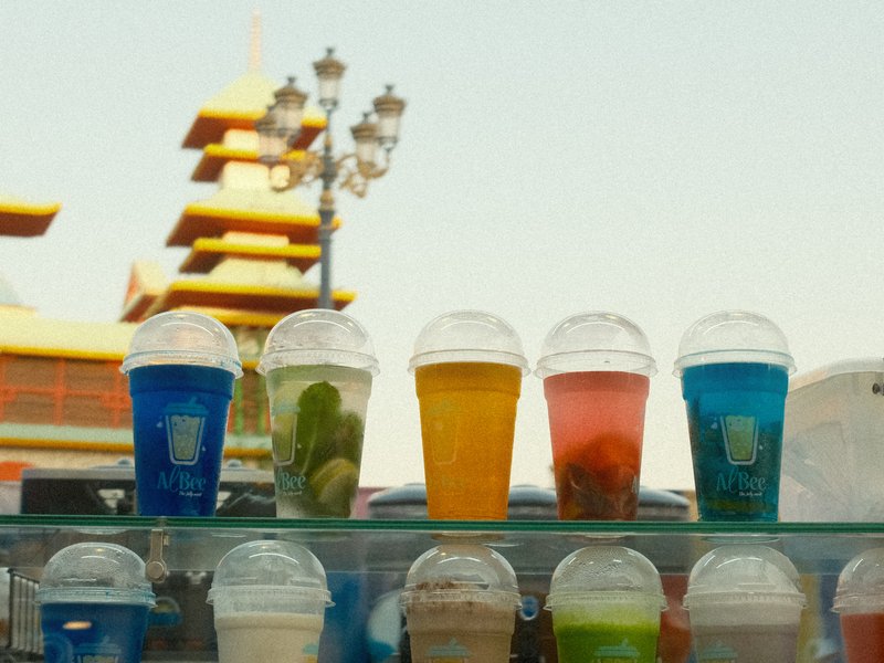 Colorful drinks in clear cups displayed in front of a pagoda-style building.