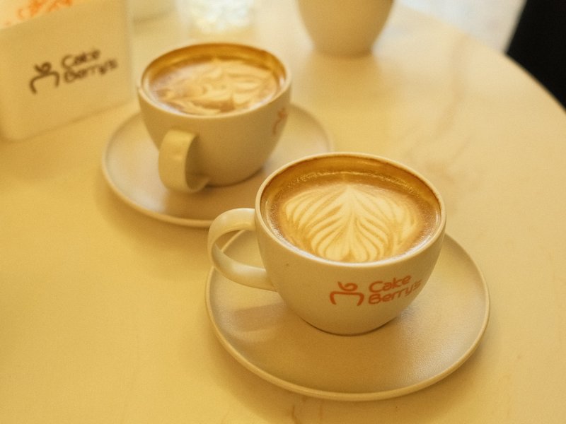 Two cups of latte art on a light-colored table with a soft background.