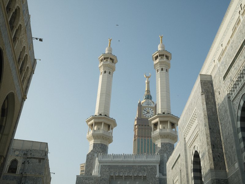 Tall minarets of a mosque against a clear blue sky, surrounded by ornate stone architecture.