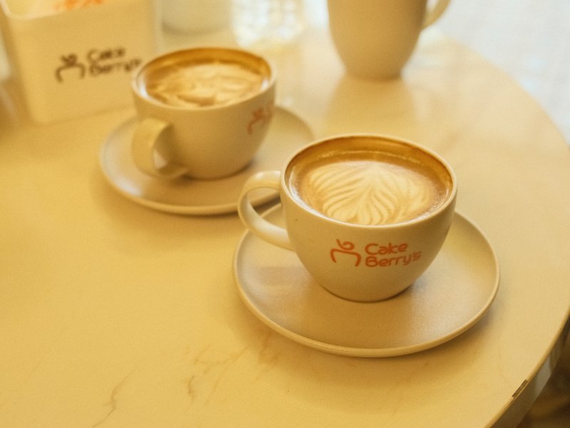 Two cups of latte art on a light-colored table with a soft focus background.