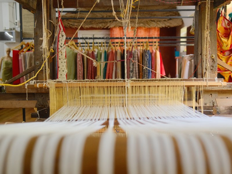A weaving loom with colorful threads hanging in the background, showcasing textile craftsmanship.
