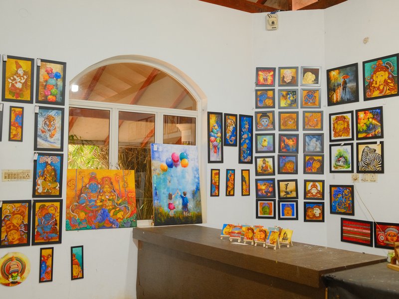 An art gallery interior showcasing colorful paintings on white walls with a wooden counter in front.