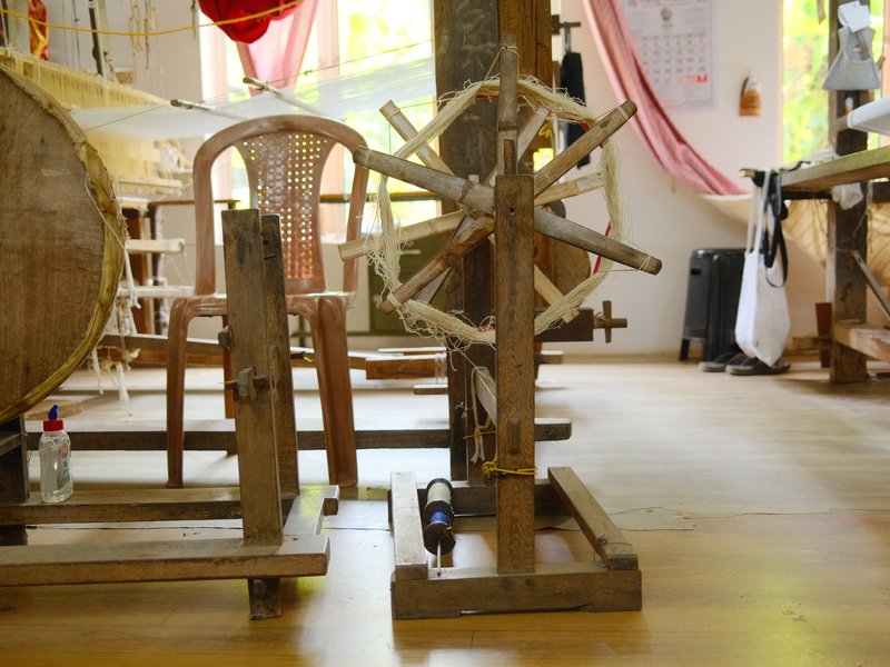 A wooden spinning wheel in a workshop setting with natural light streaming in through a window.