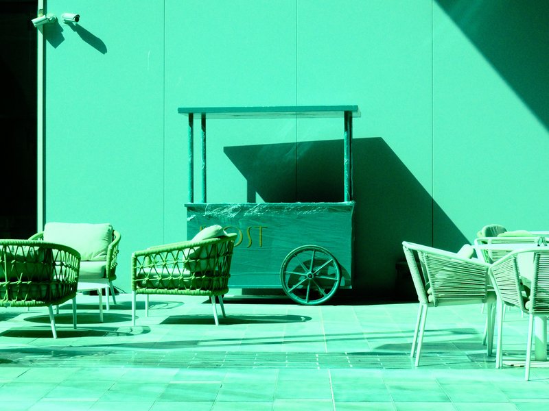 A turquoise food cart beside light-colored chairs in a bright, shadowed outdoor setting.