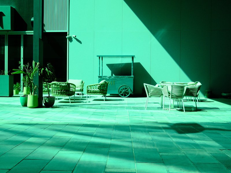 A modern outdoor seating area with green tones and long shadows cast on the tiled floor.