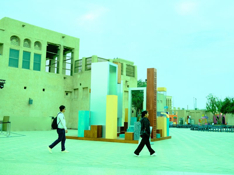Two people walking past colorful abstract sculptures in an outdoor urban setting.