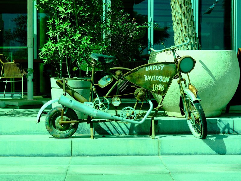 A vintage motorcycle parked beside a large planter in an urban setting with greenish tones.