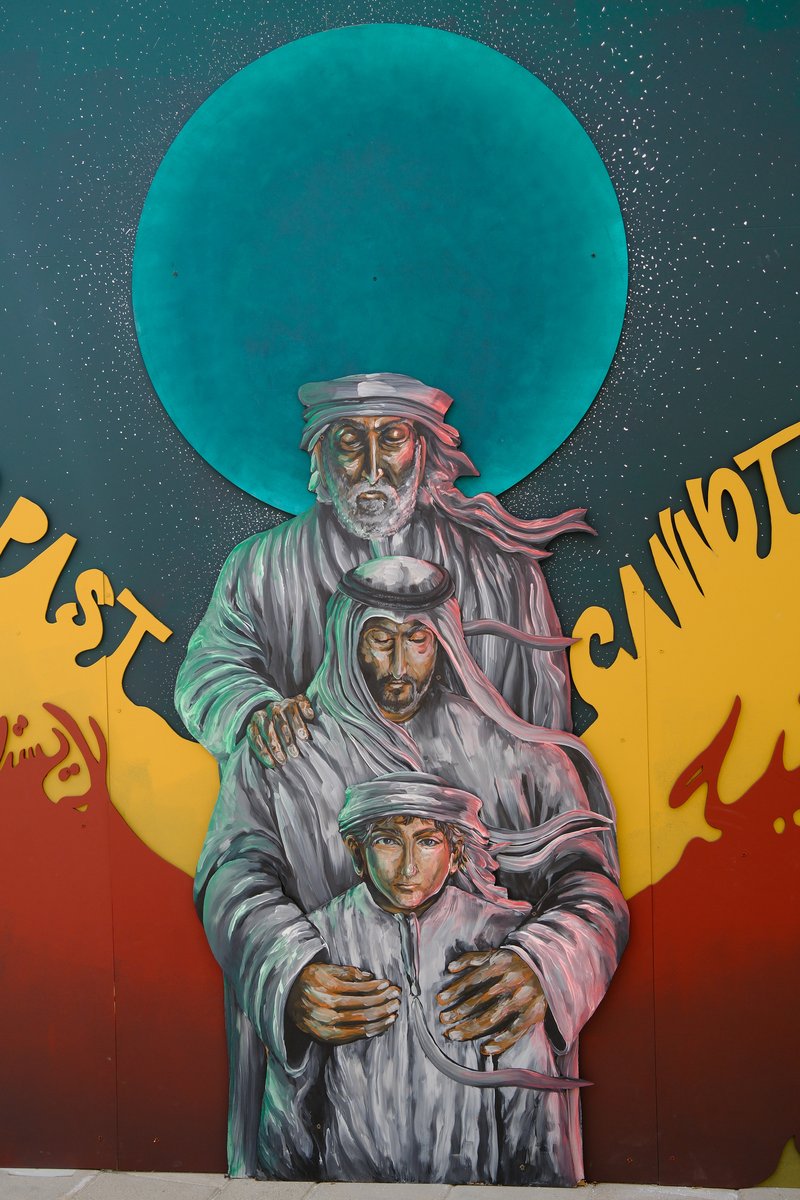 A mural depicting three figures, an elder and two younger individuals, against a colorful background.