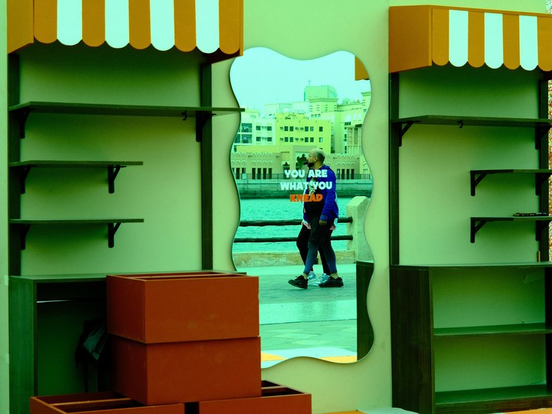 A reflection of a person walking past colorful shelves in an outdoor setting.
