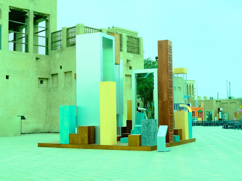 Colorful abstract sculpture in an outdoor urban setting with buildings in the background.